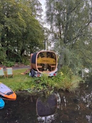 Bakvisning med panoramaglass av TimberIN Nordic Square mobilbadstue på tilhenger ved en innsjø